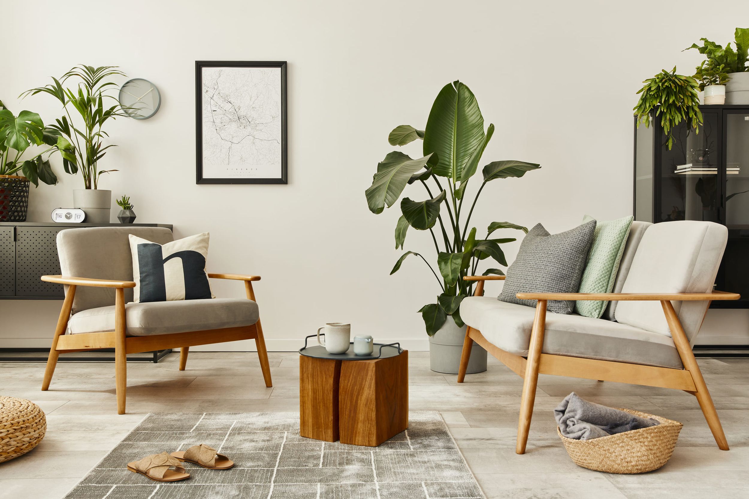 Wohnzimmer mit zwei hellgrauen Sesseln mit Holzgestell, kleinem Holztisch, Pflanzen und Wanddekoration